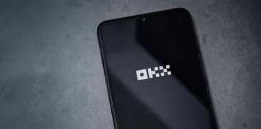 OKX app launch screen on smartphone on dark marble stone background