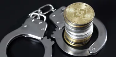 Stack of binance coins and handcuffs over black background