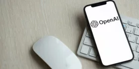 OpenAI logo on iPhone display screen with apple keyboard and mouse on table