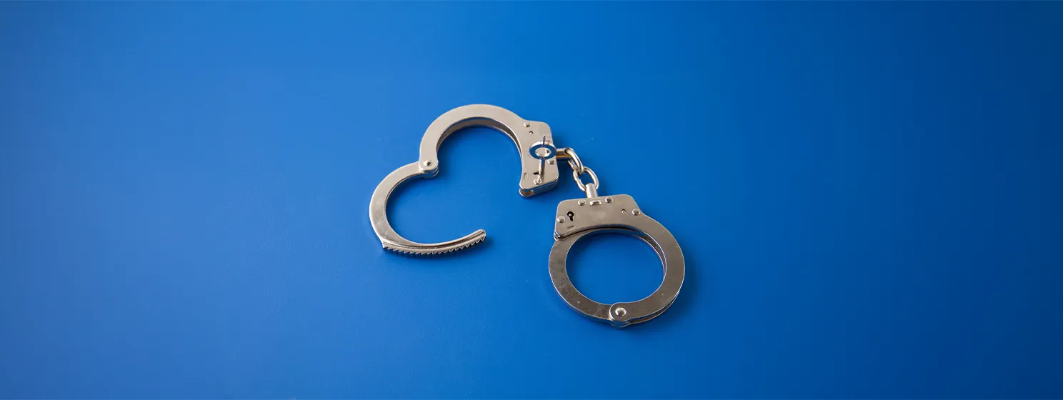 Open handcuffs with key on blue background