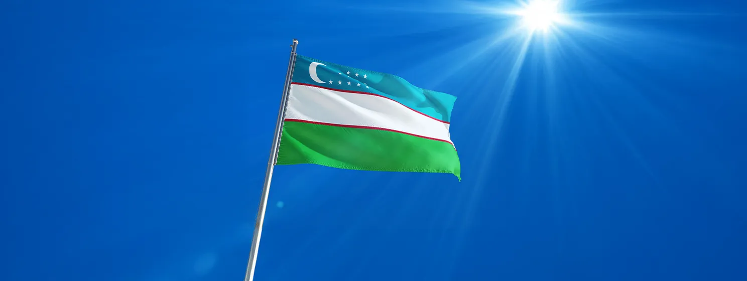 Uzbekistan National Flag Waving on pole against deep blue sky