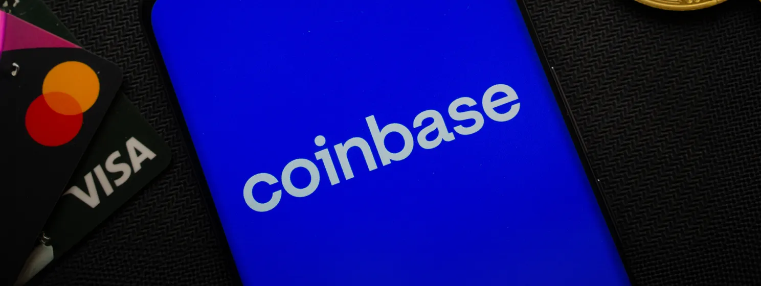 Smartphone displaying Coinbase logo surrounded by Bitcoin coins and payment cards