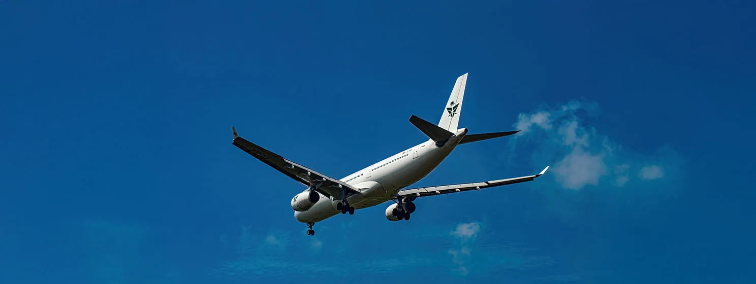 A Saudia Airline aircraft used for Hajj pilgrims is captured mid-flight with landing gear extended, soaring against a backdrop of blue sky and clouds.