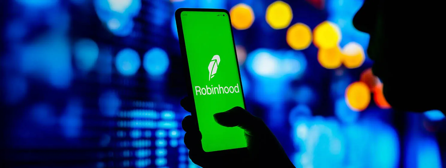 A woman silhouette holds a smartphone with the Robinhood Markets logo displayed on the screen.
