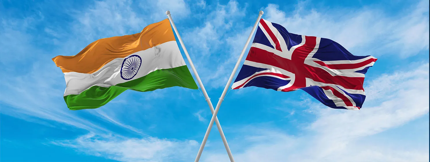 Crossed national flags of India and Great Britain flag waving in the wind at cloudy sky.