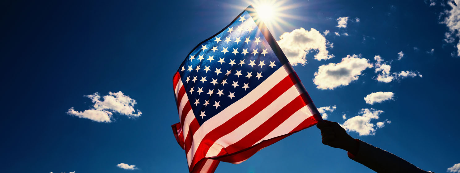 Waving USA flag in hand against blue sky