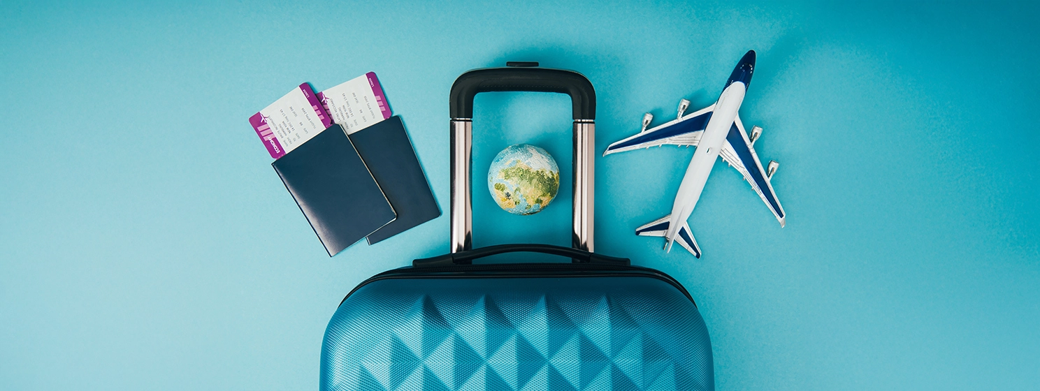 Top view of globe and plane models, travel bag and passports with tickets on blue background.