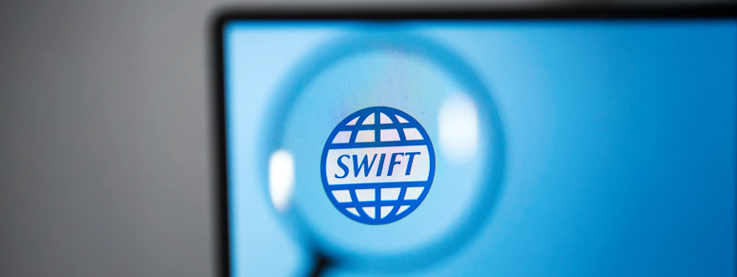SWIFT logo on a computer monitor under a magnifying glass.